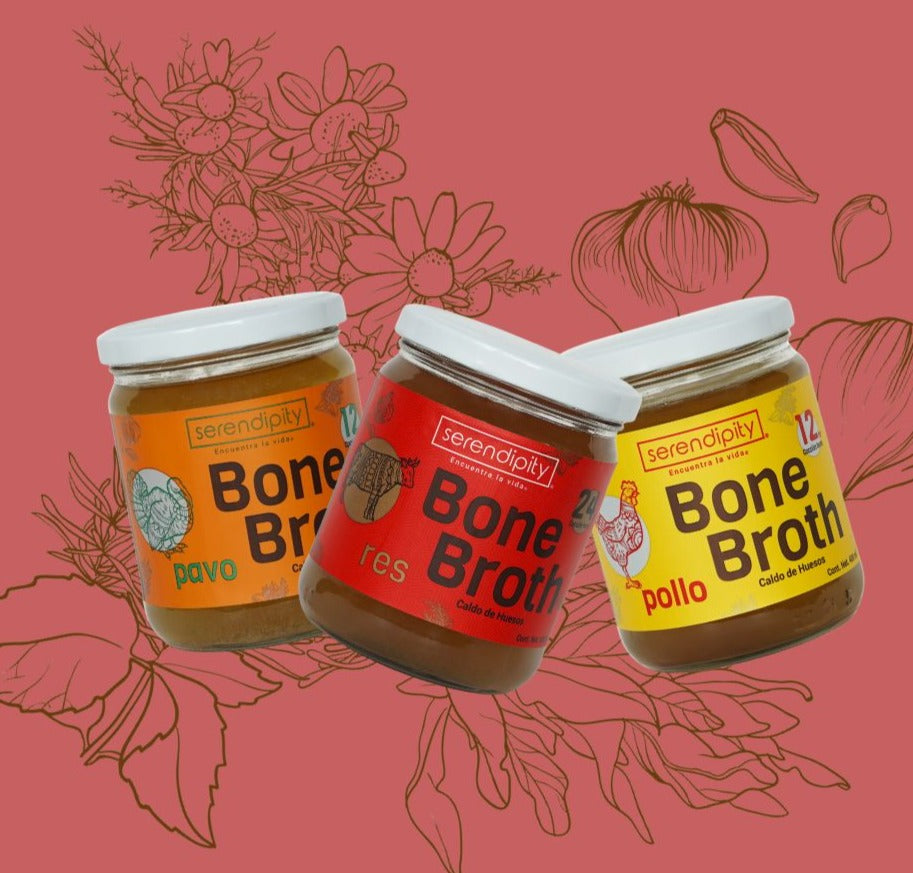 Frasco de caldos de hueso de res pollo y pavo de la marca 'serendipity' con una etiqueta blanca, flotando frente a un fondo rosa con ilustraciones de hierbas. La etiqueta muestra  el texto 'Bone Broth, cordero, Caldo de Huesos'